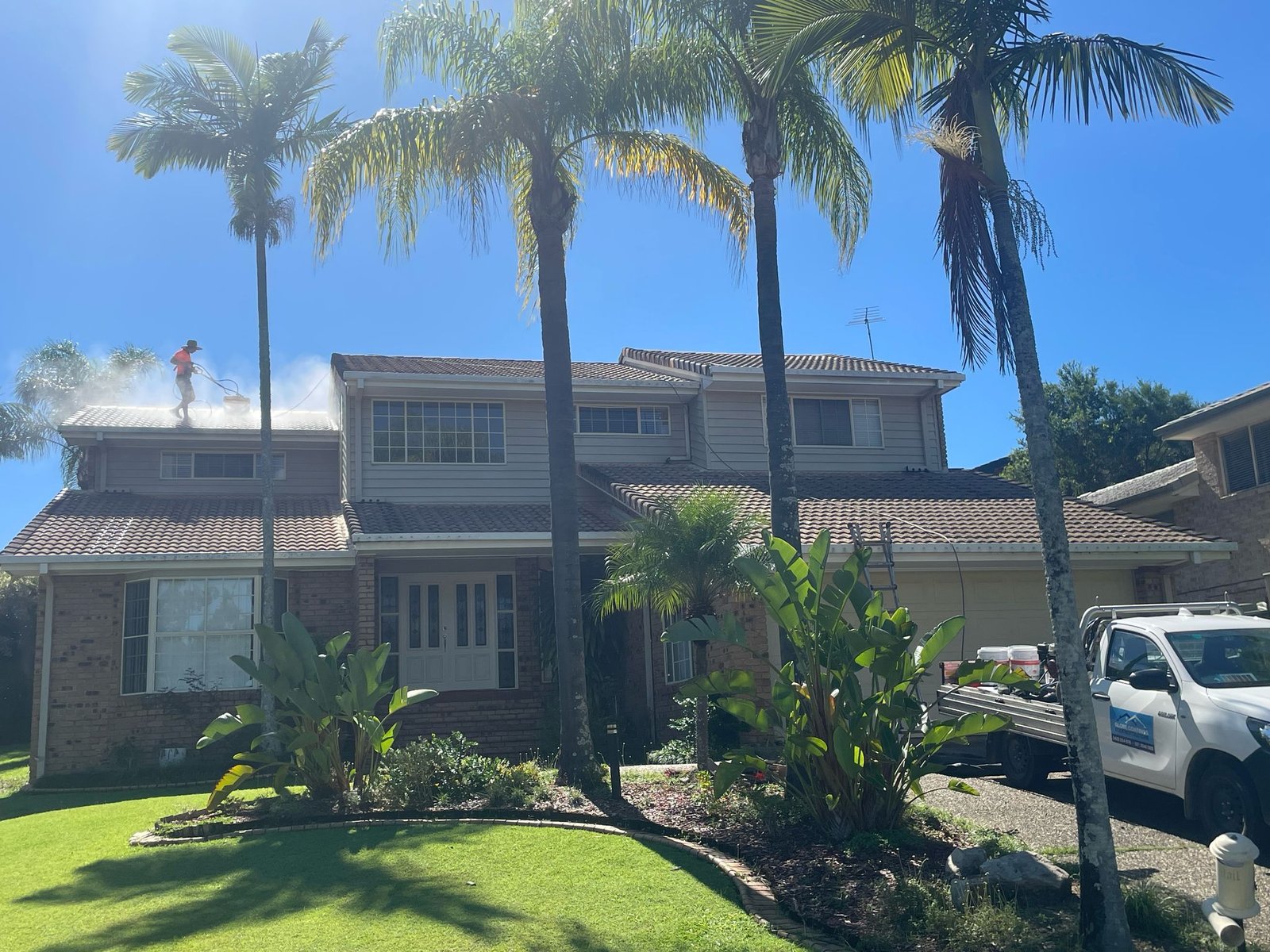 Roofer pressure cleaning the tile roof of a large Brisbane home
