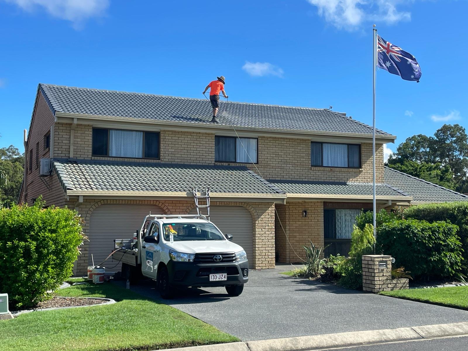 Roofer working along the ridge of a grey concrete tile roof mid-clean